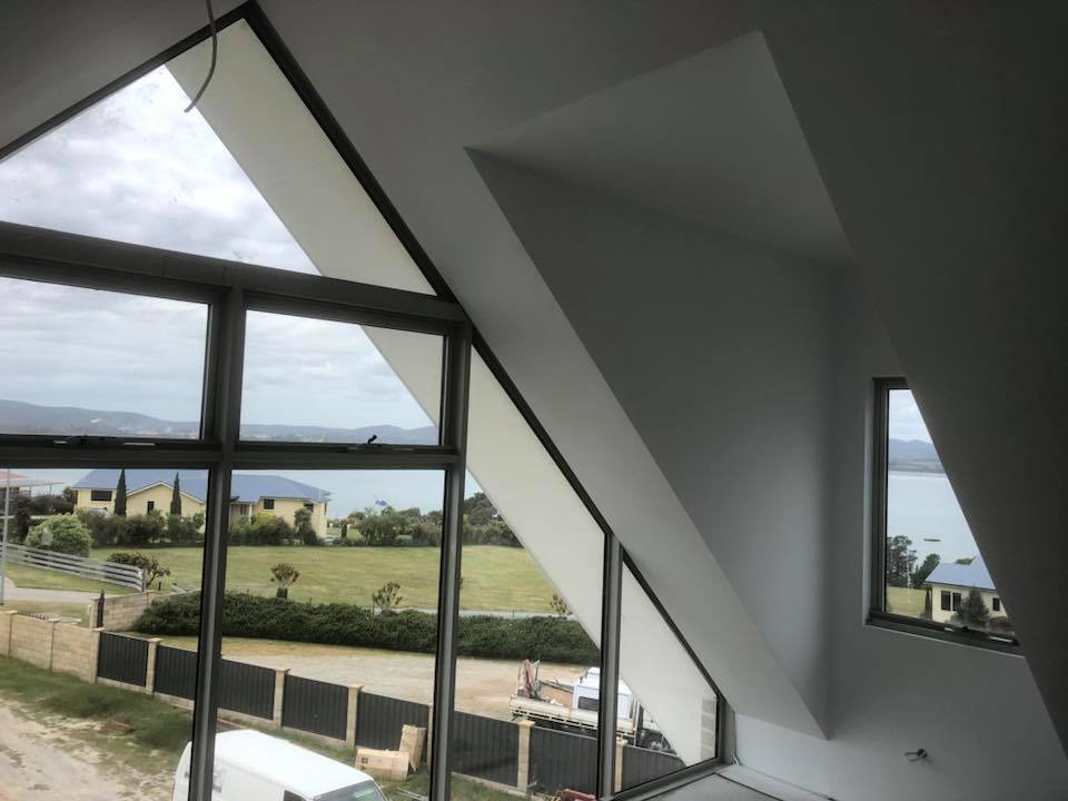 Plastered raked ceiling and angled walls around large windows overlooking water
