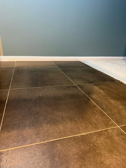 Close-up of large dark grey floor tiles meeting a blue painted wall