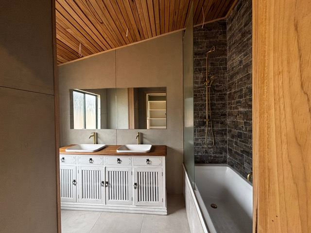 Bathroom with double basin vanity, bath, dark stone feature wall and timber ceiling