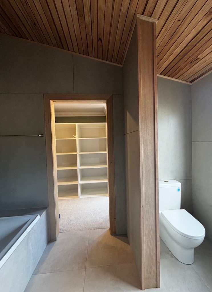 Bathroom with toilet and built-in bath, opening into a walk-in robe with shelving