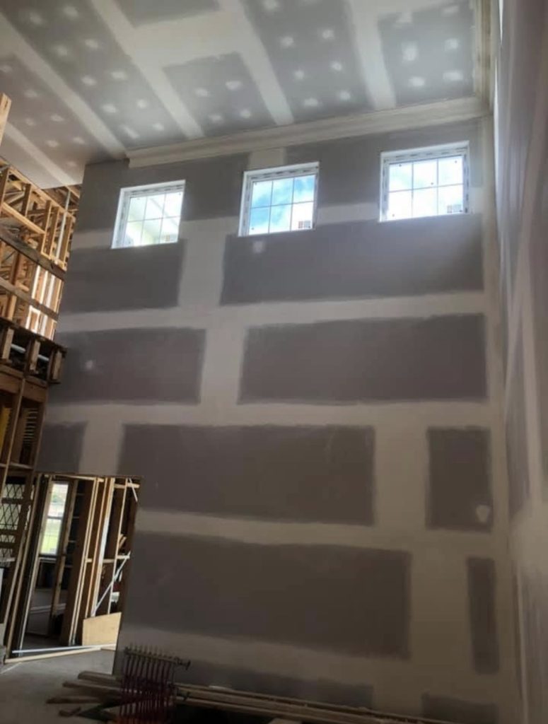 Tall plasterboard wall with set joints below three high windows